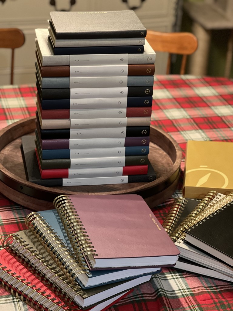 Stack of Full Focus Planners in various colors on a wooden tray, with spiral-bound planners in front